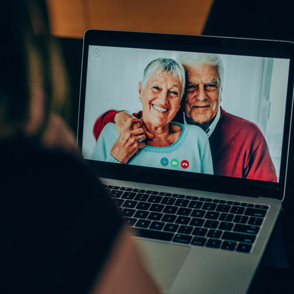 Persona en videollamada con una pareja mayor en un portátil, asesorando sobre ampliación de capital online.