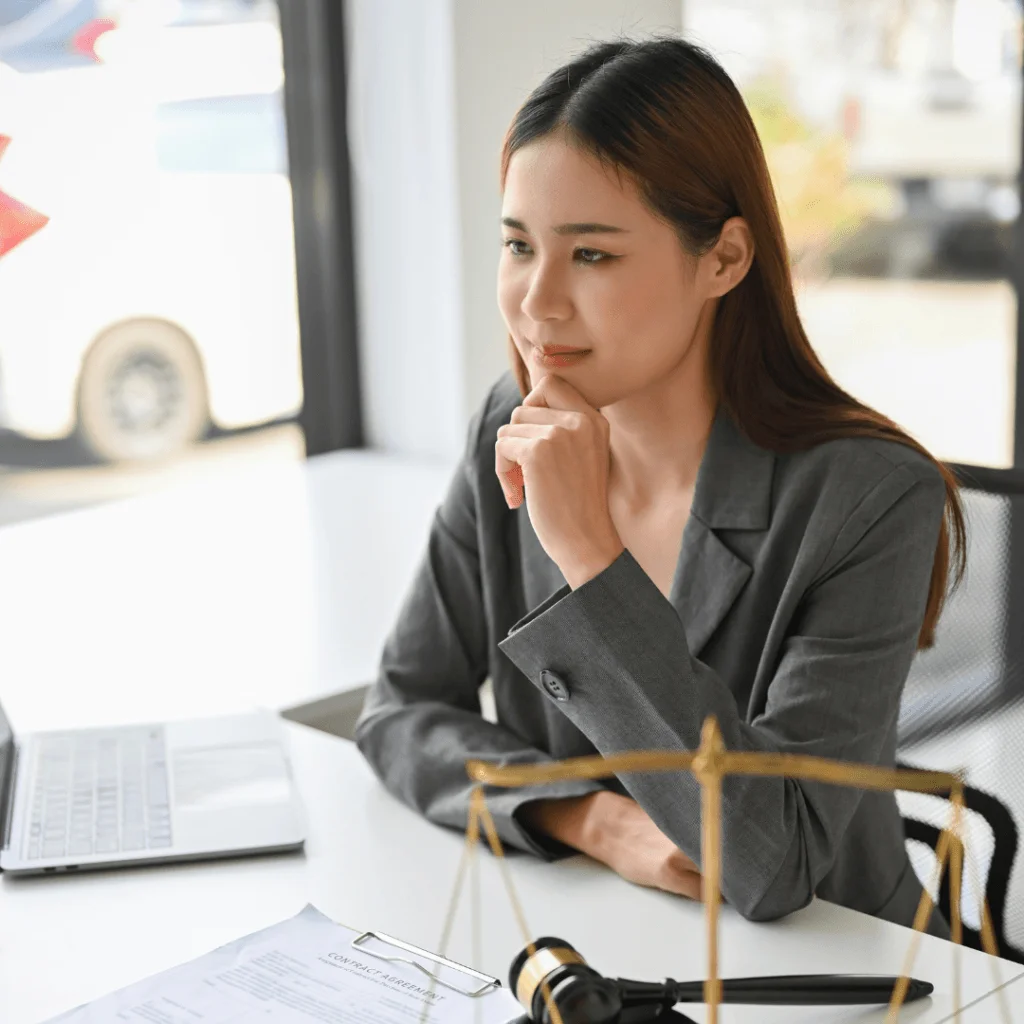 Abogada pensativa en su escritorio con portátil y documentos legales, analizando la disolución y liquidación de empresas online.